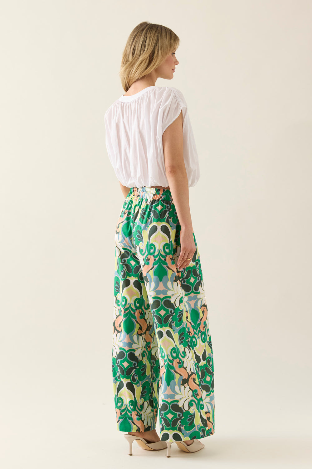 Woman wearing a isle of mine white top and green floral pants on a plain background