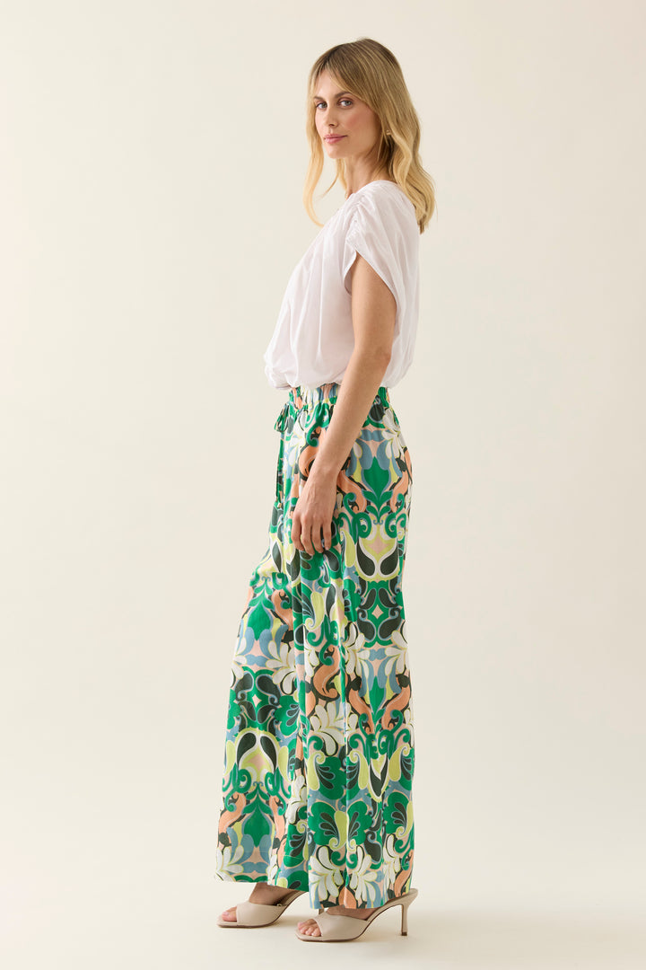Woman wearing a white isle of mine top and colorful patterned pants on a plain background