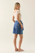 Woman wearing a beige top and isle of mine blue denim shorts on a plain background