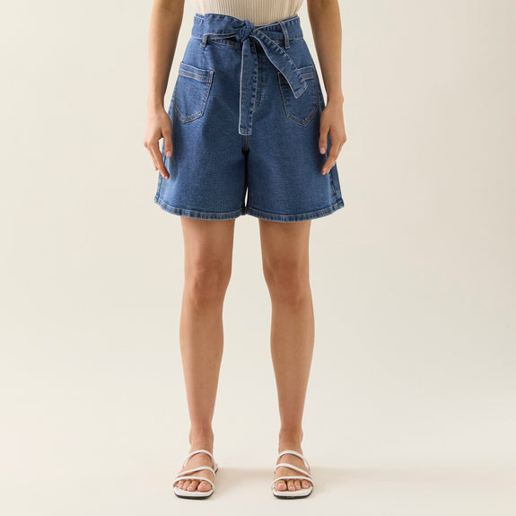 Woman wearing a white top and isle of mine blue denim shorts on a plain background