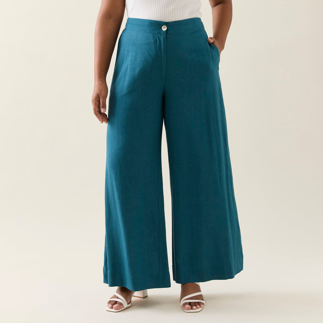 Woman wearing a white top and teal wide-leg pants on a plain background
