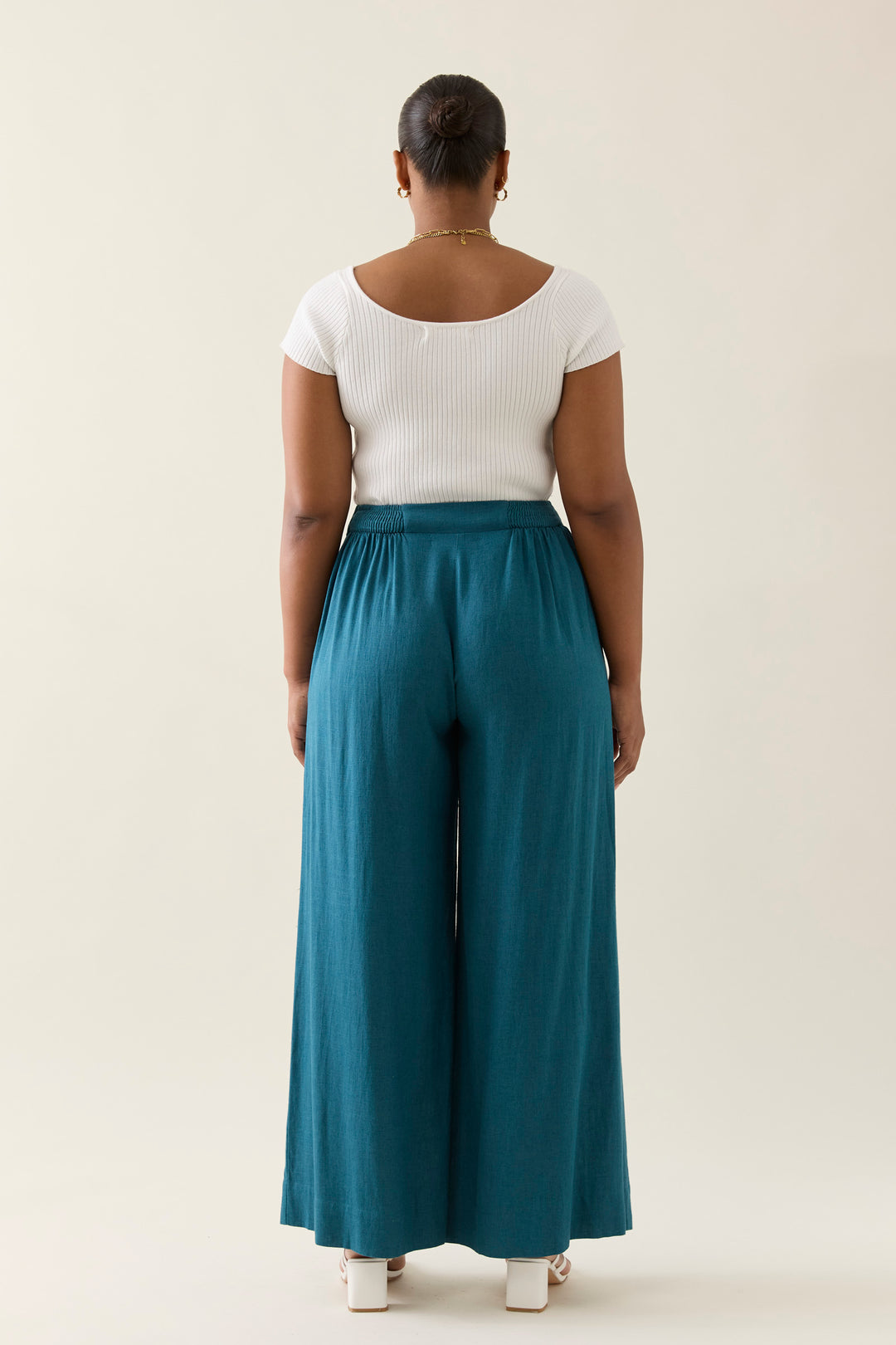 Person wearing a white top and teal isle of mine wide-leg pants on a beige background