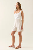 Woman wearing a white tank top and beige isle of mine shorts against a plain background