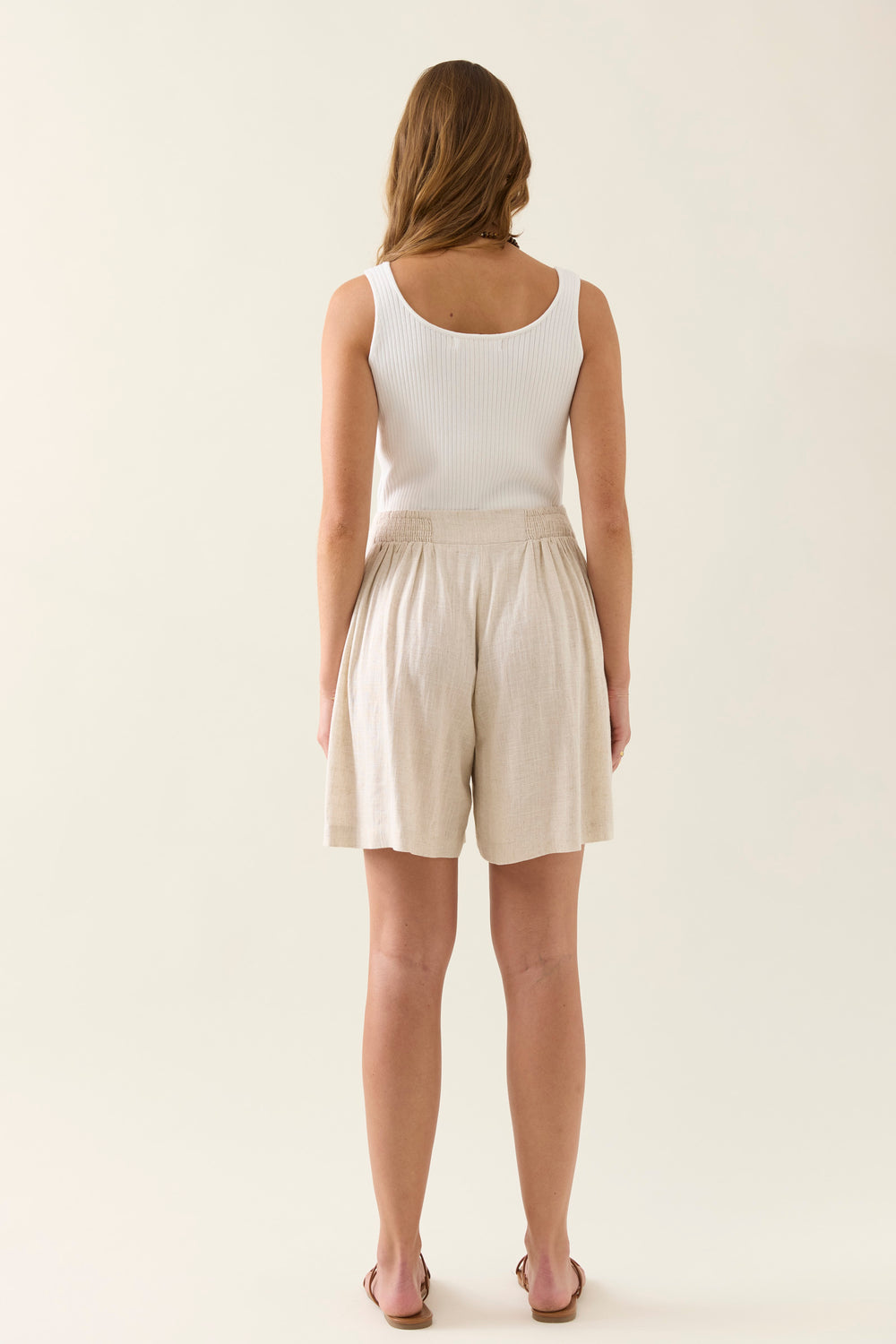 Woman wearing a white tank top and beige isle of mine shorts on a plain background
