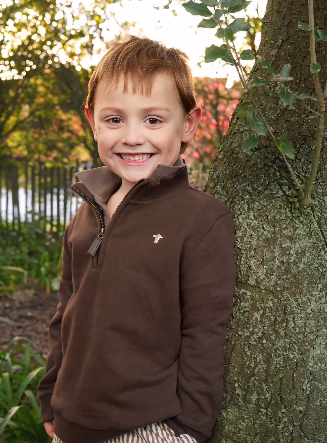 Child wearing a brown fleece leaning against a tree outdoors