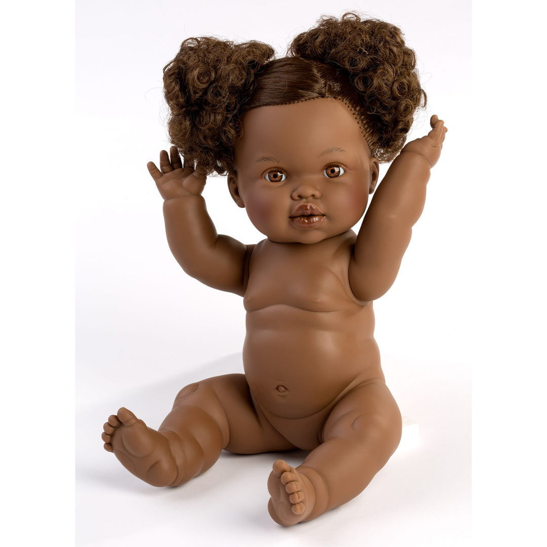 A realistic sitting baby doll with medium brown skin, curly brown hair styled in two buns, and raised arms, photographed against a plain white background.