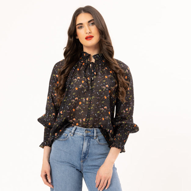 Woman wearing a patterned blouse and blue jeans on a white background