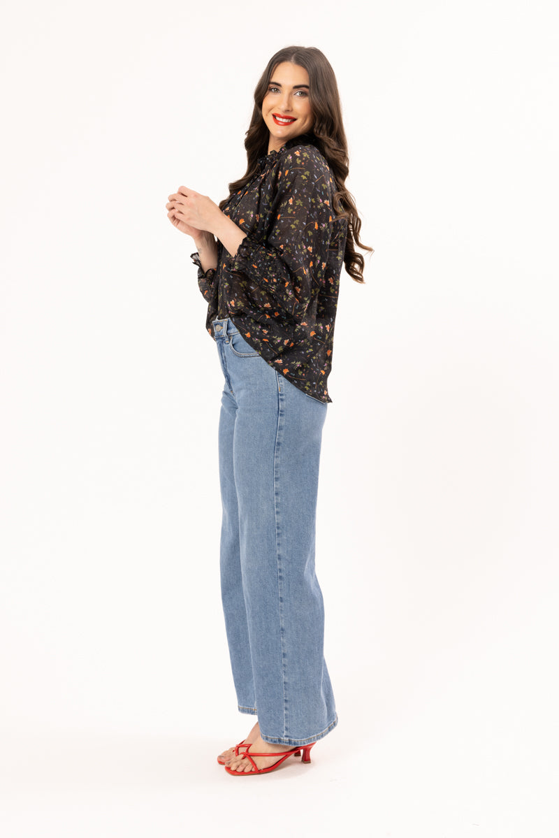 Woman wearing a black floral blouse and blue jeans on a white background