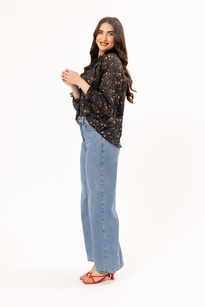 Woman wearing a black floral blouse and blue jeans on a white background