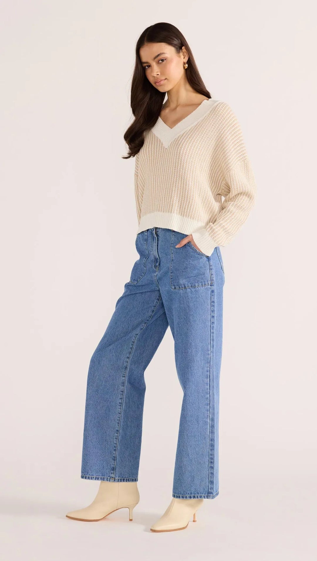 Woman wearing a Minkpink cream sweater and blue jeans on a white background