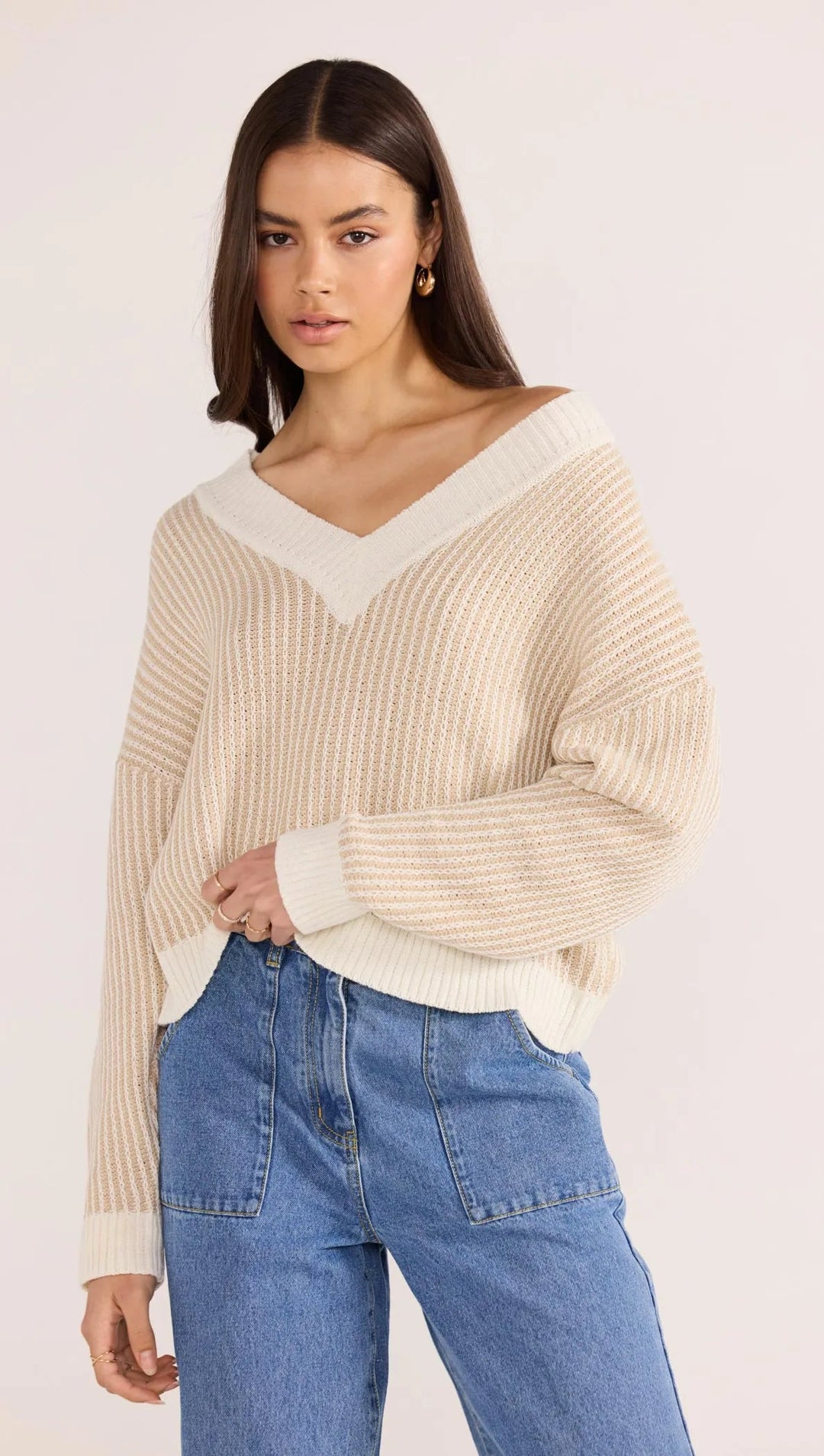 Woman wearing a beige sweater and blue jeans on a white background