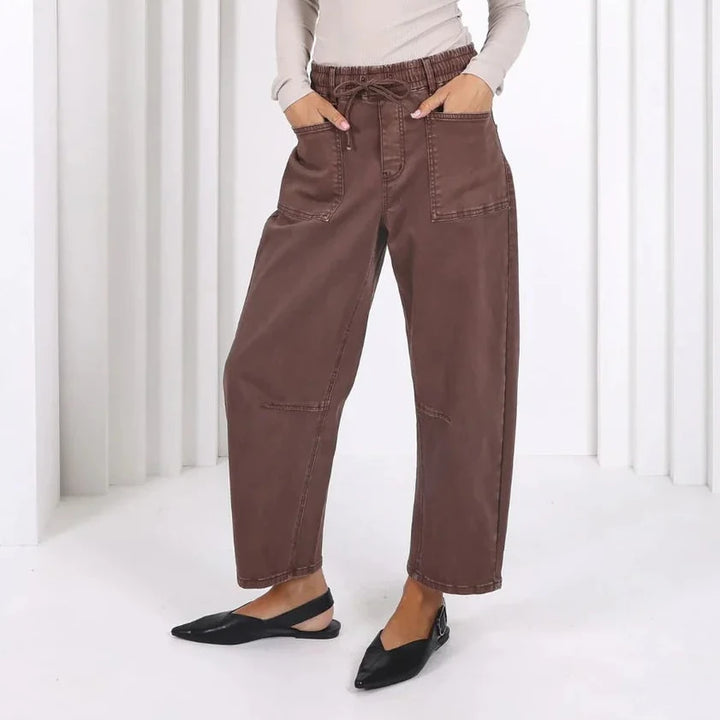 Woman wearing brown pants and a light top standing in a white archway.