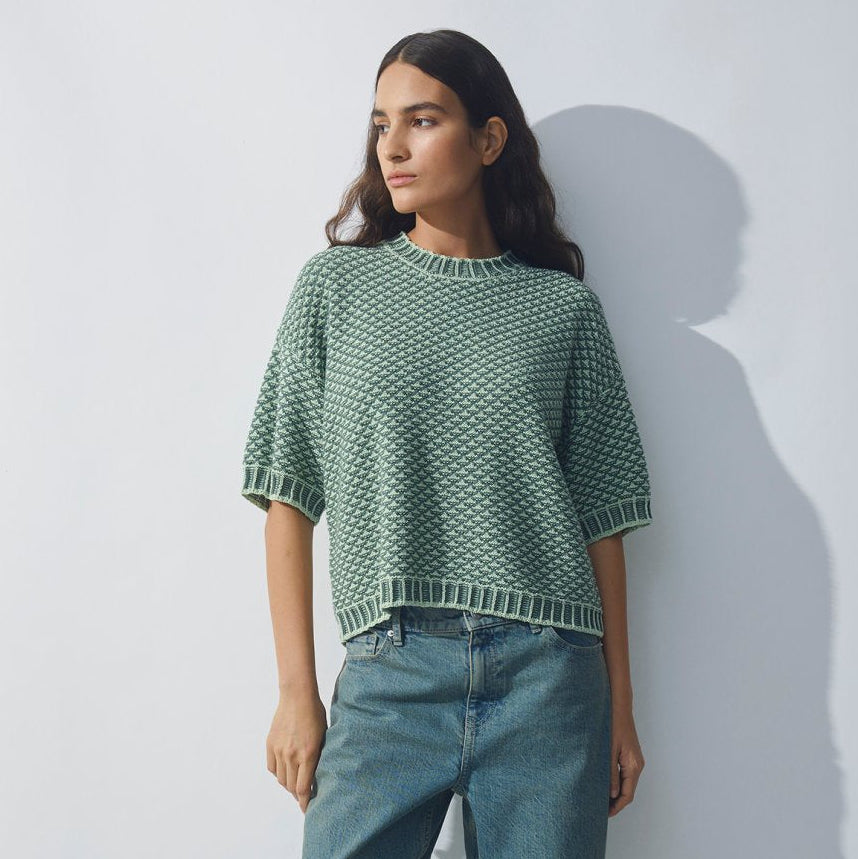 Woman wearing a green patterned top and blue jeans against a white background