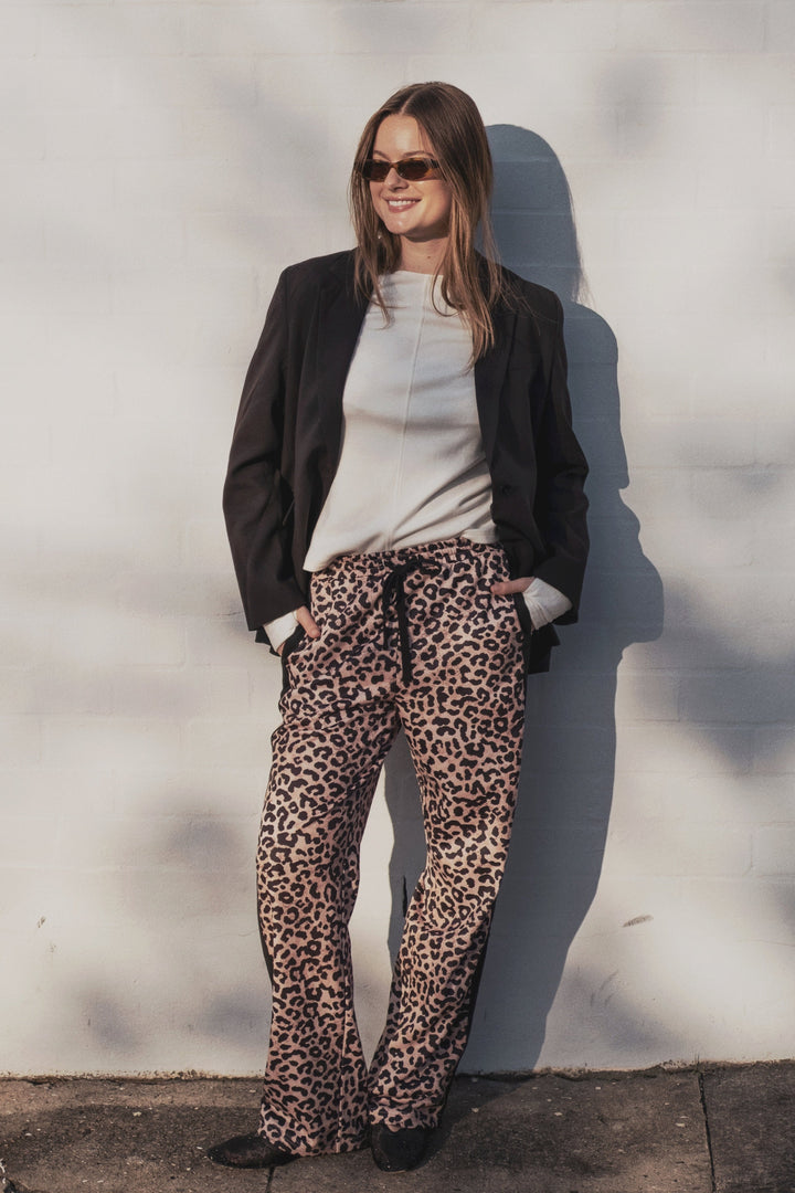 Person wearing a black jacket, white shirt, and leopard print pants against a light background