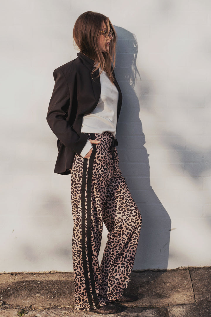 Person wearing a black blazer, white shirt, and cartel & willow leopard print pants against a light background