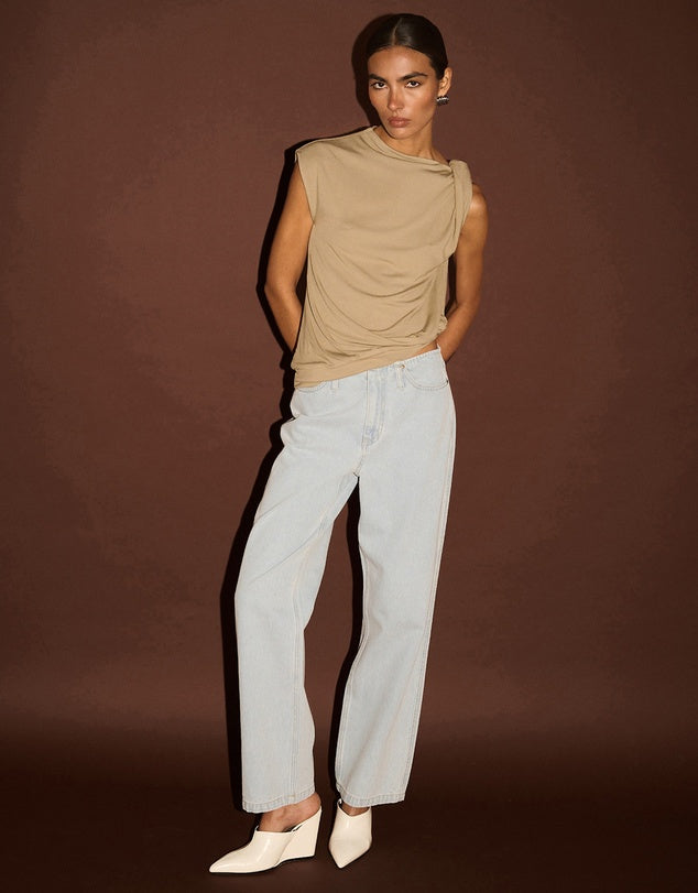 Woman wearing a beige sleeveless top and light blue jeans against a brown background