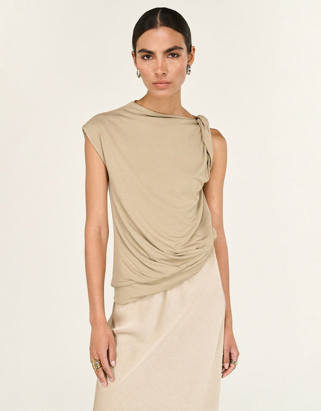 Woman wearing a beige sleeveless top with a draped design on a plain background