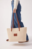 Person holding a beige tote bag with brown straps on a white background
