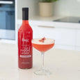 Red cocktail mixer bottle labeled 'fling' next to a glass of pink cocktail on a kitchen counter.