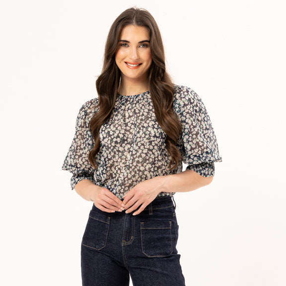 Woman wearing a floral blouse and dark jeans on a white background