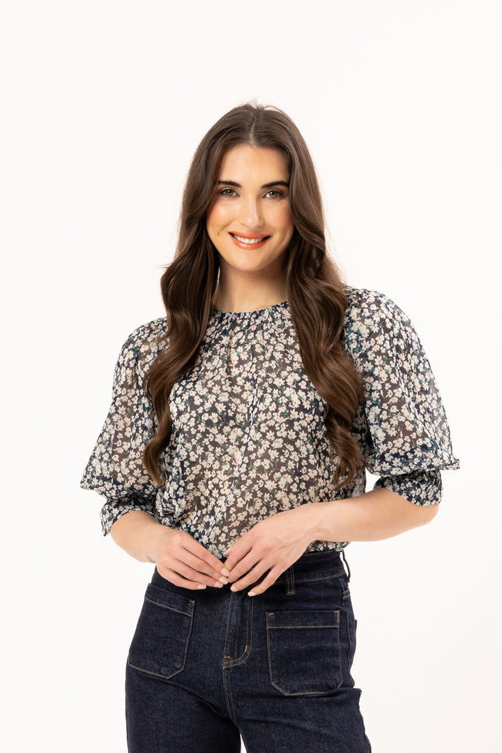 Woman wearing a floral blouse and dark jeans on a white background
