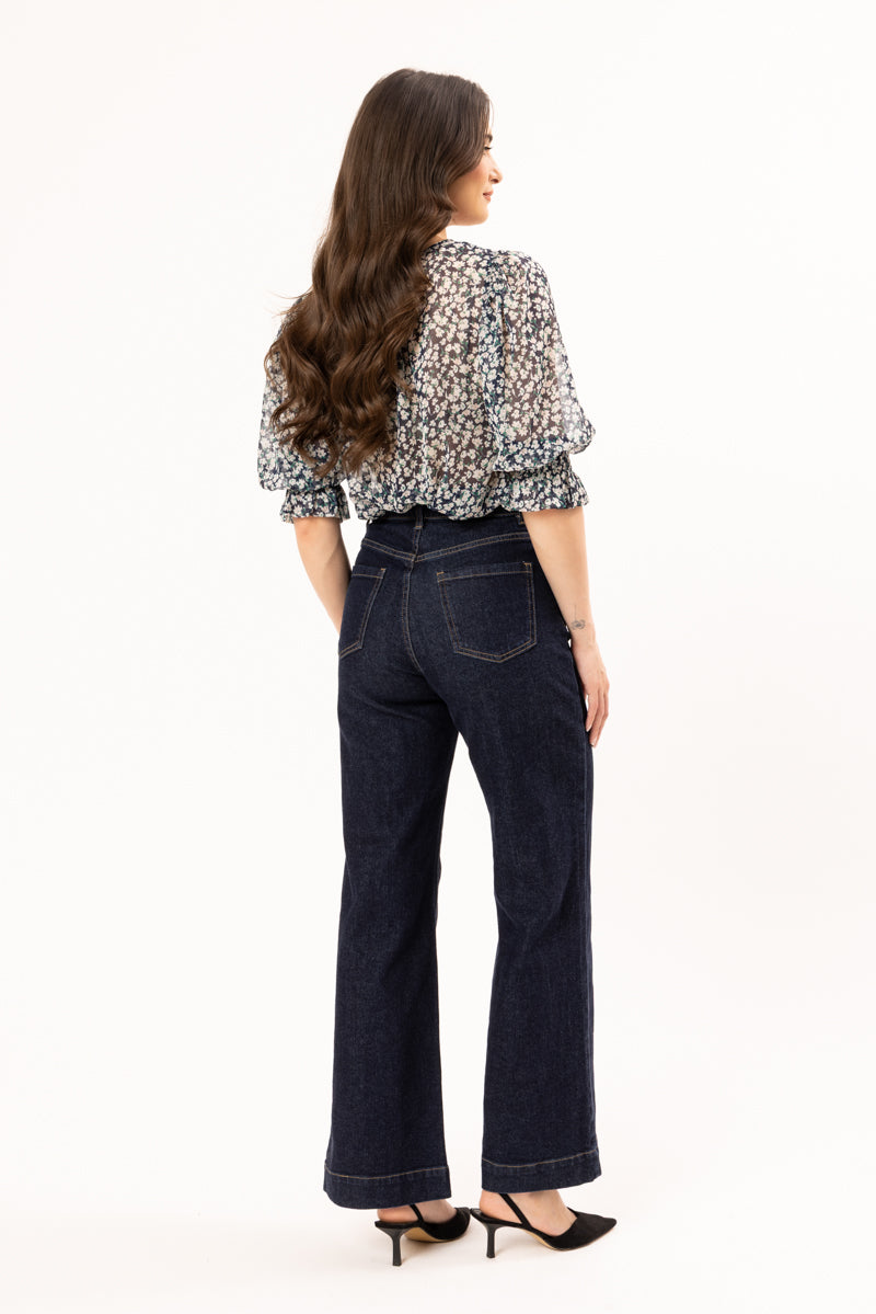 Woman wearing a patterned blouse and dark jeans on a white background