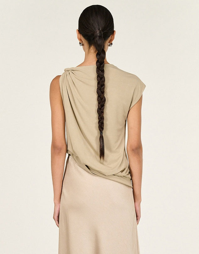 Woman wearing a beige sleeveless top with a braided hairstyle on a light background