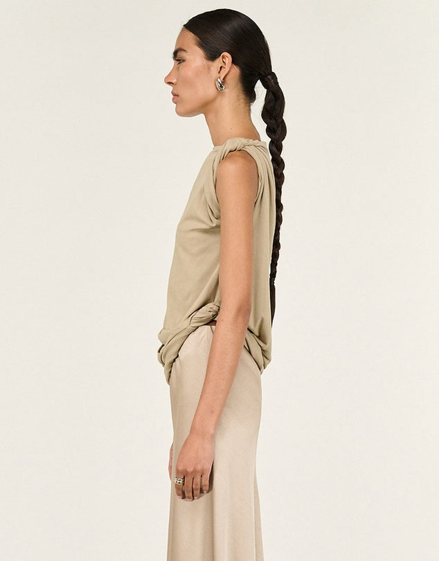 Woman wearing a beige sleeveless top and pants against a white background