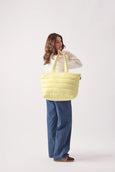 Person holding a large light yellow quilted tote bag against a white background