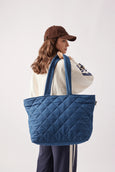 Person carrying a large blue quilted tote bag on a white background