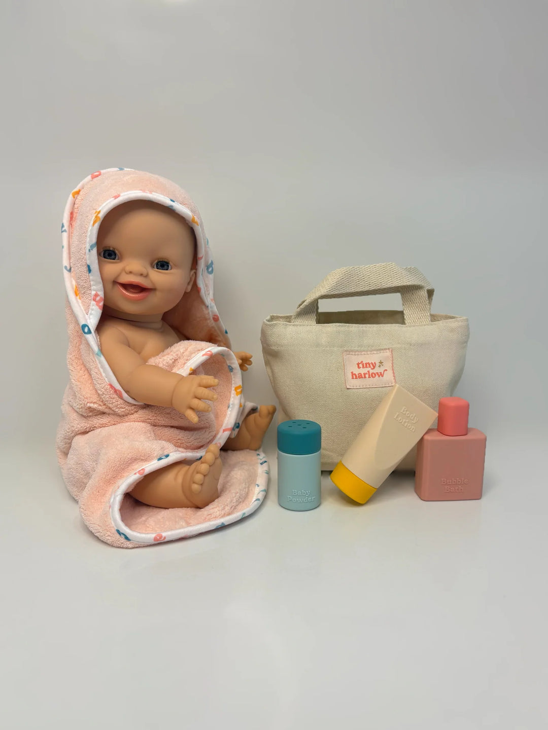Baby doll wrapped in a pink towel with a bag and toys on a white background