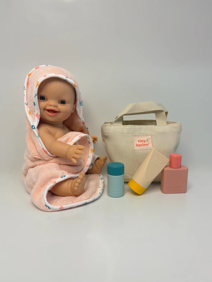 Baby doll wrapped in a pink towel with a bag and toys on a white background