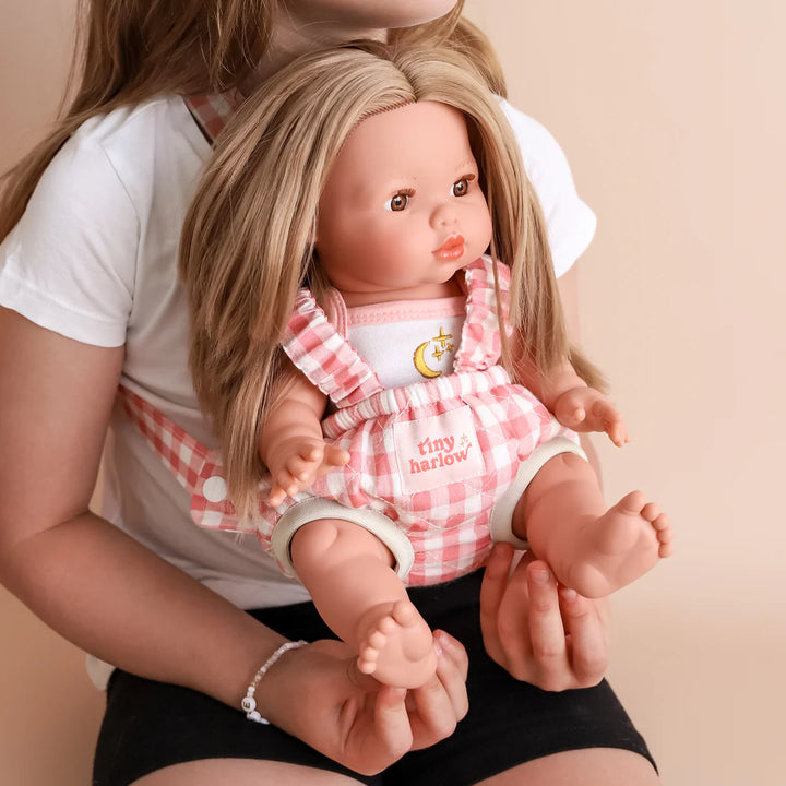 Person holding a doll wearing a pink checkered outfit with 'tiny harlow' branding.