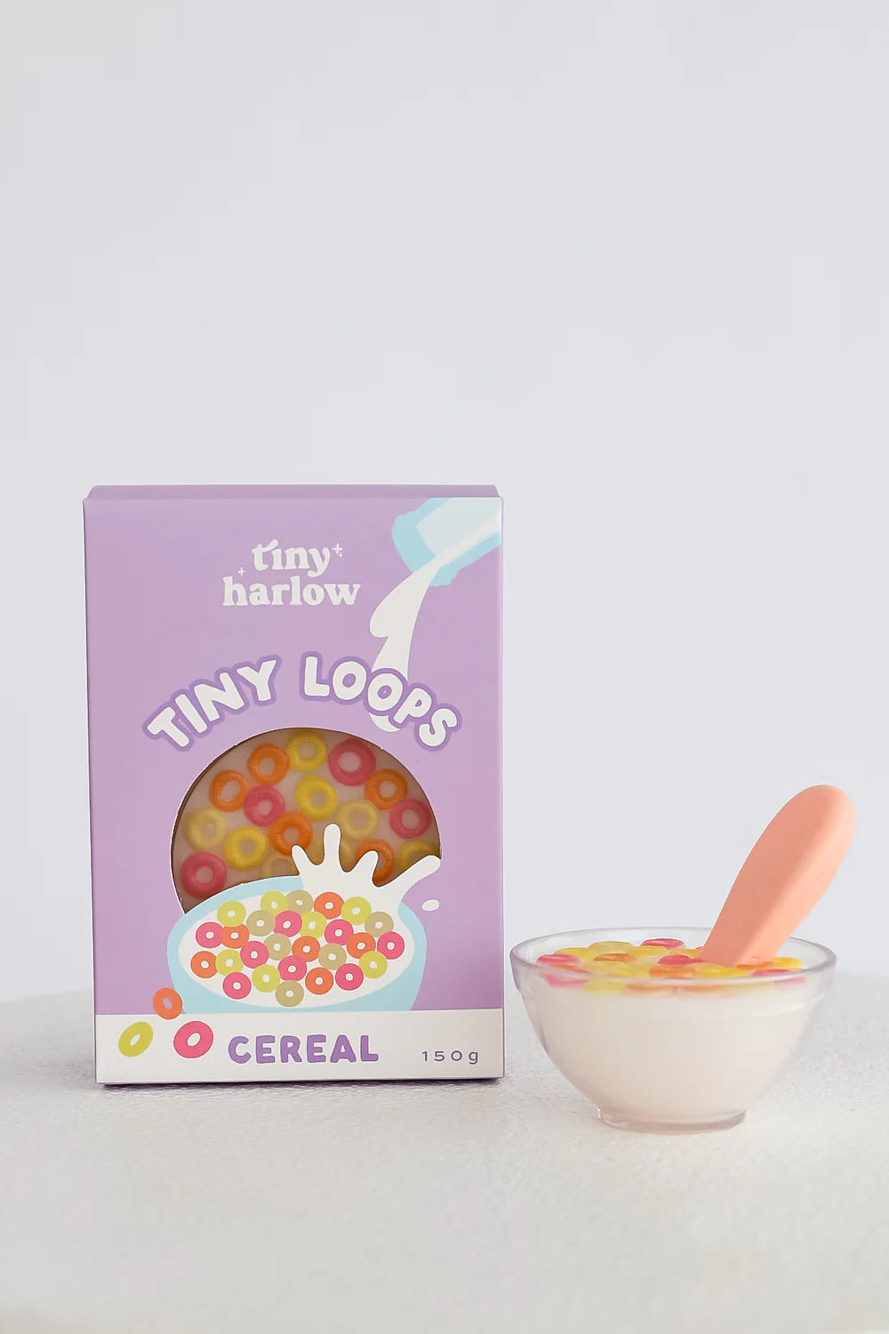 Box of 'tiny harlow' Tiny Loops cereal with a bowl of cereal and spoon on a light gray background