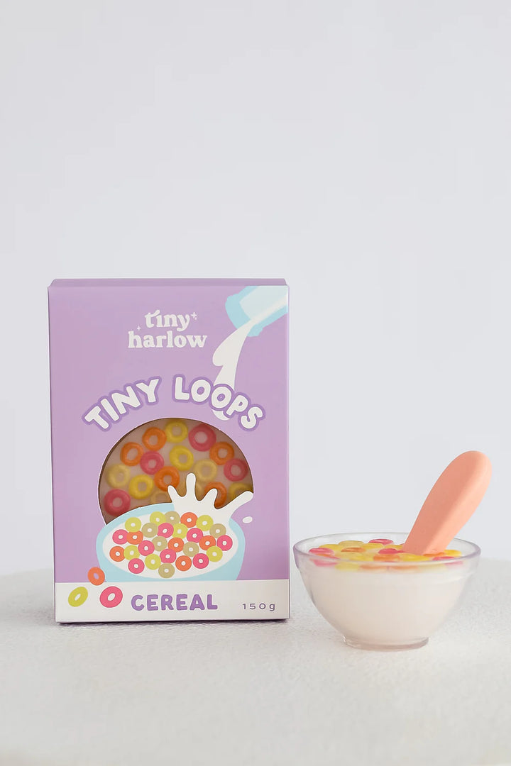 Box of 'tiny harlow' Tiny Loops cereal with a bowl of cereal and spoon on a light gray background