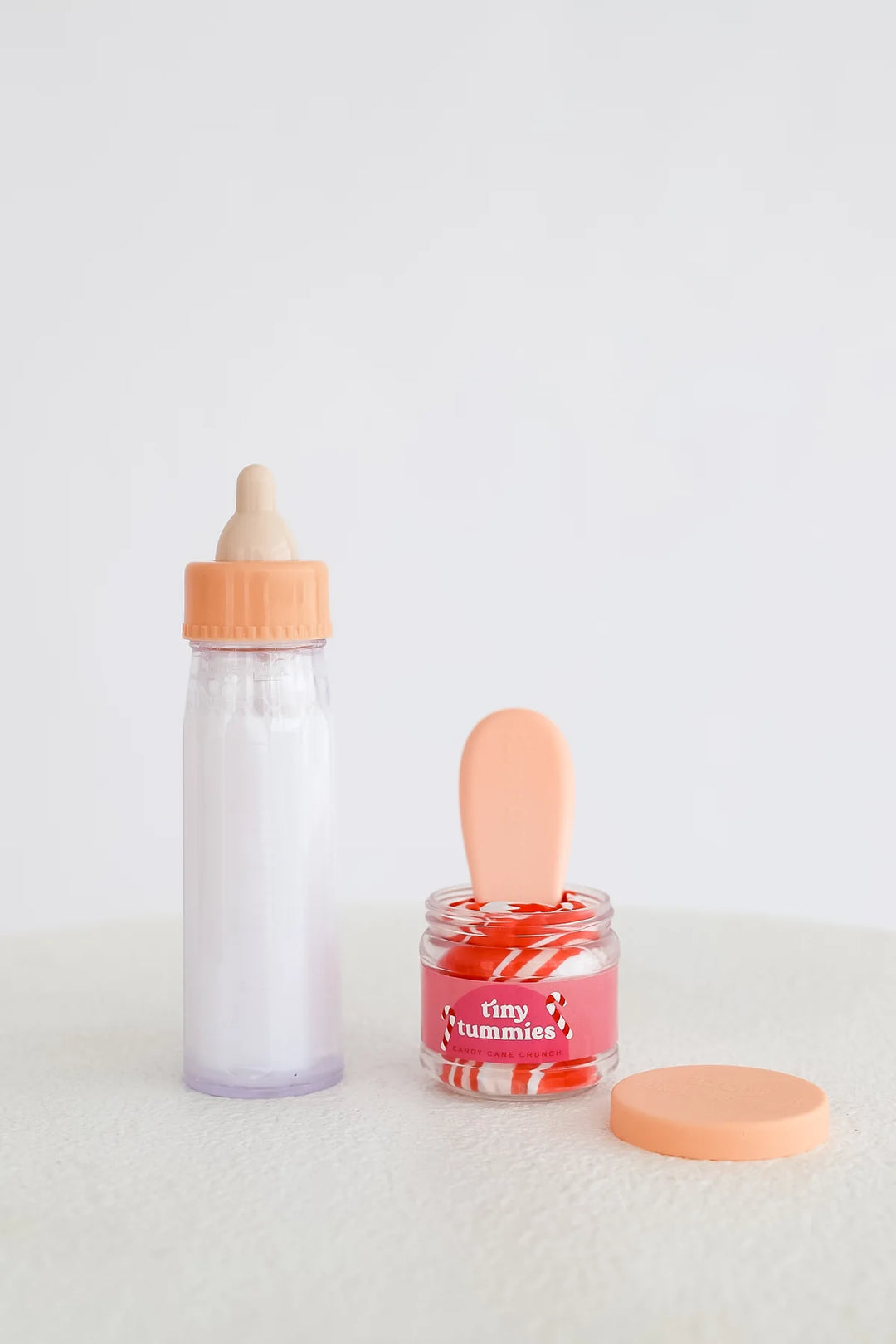 Baby bottle and jar with pink lid on a light gray background