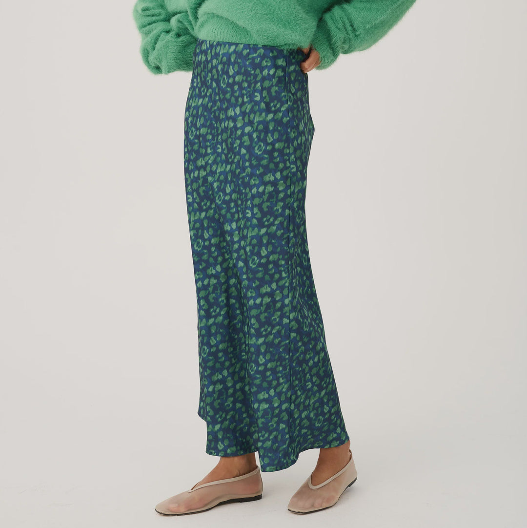 Woman wearing a green sweater and patterned skirt on a white background