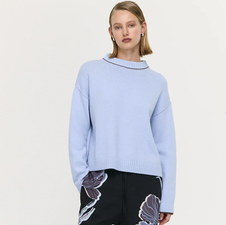 Woman wearing a light blue sweater with black trim on a plain background