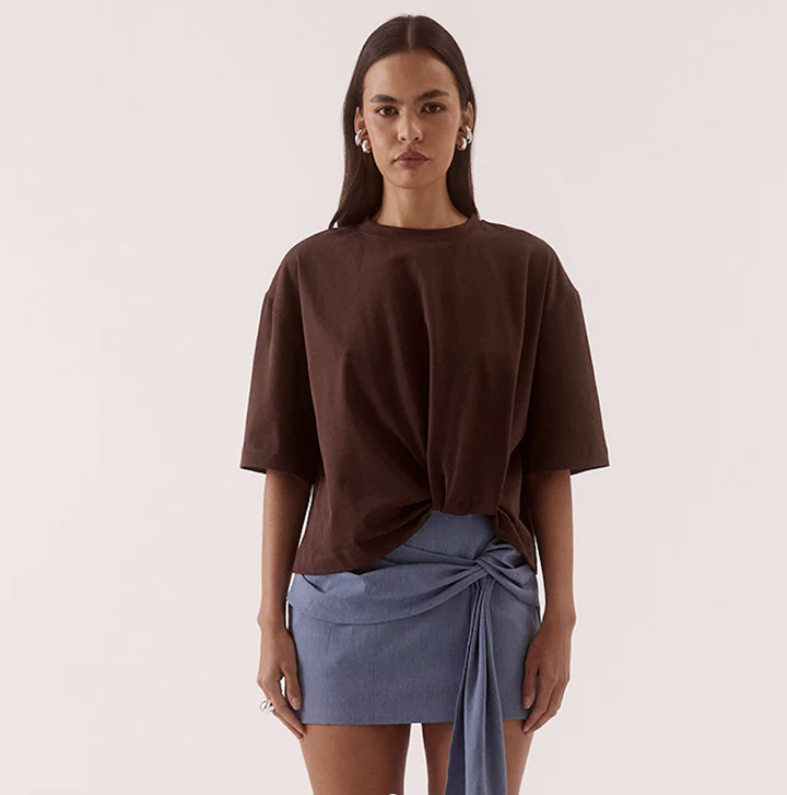 Woman wearing a brown top and blue skirt on a plain background