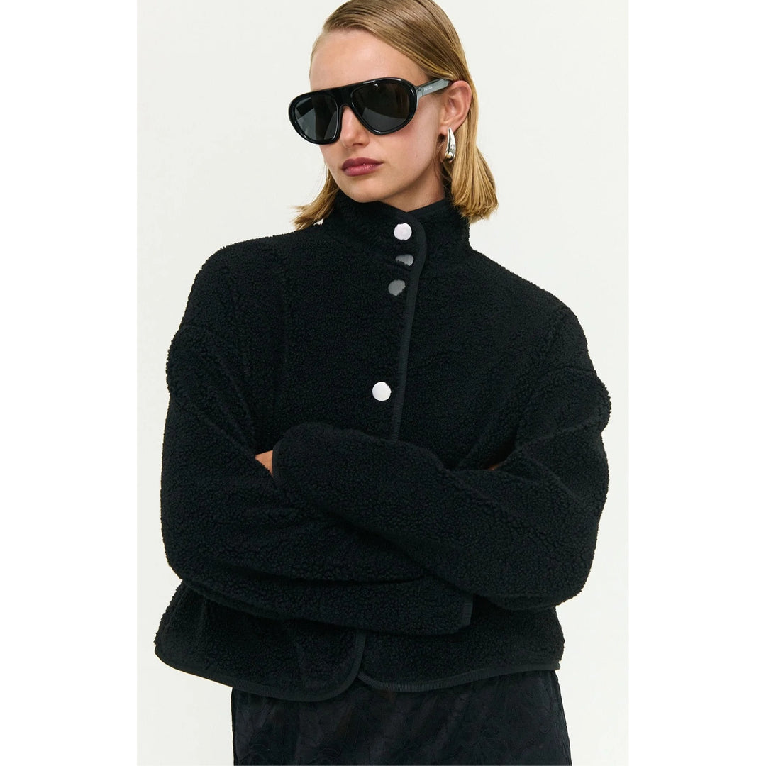 Person wearing a black textured sweater with white buttons on a white background