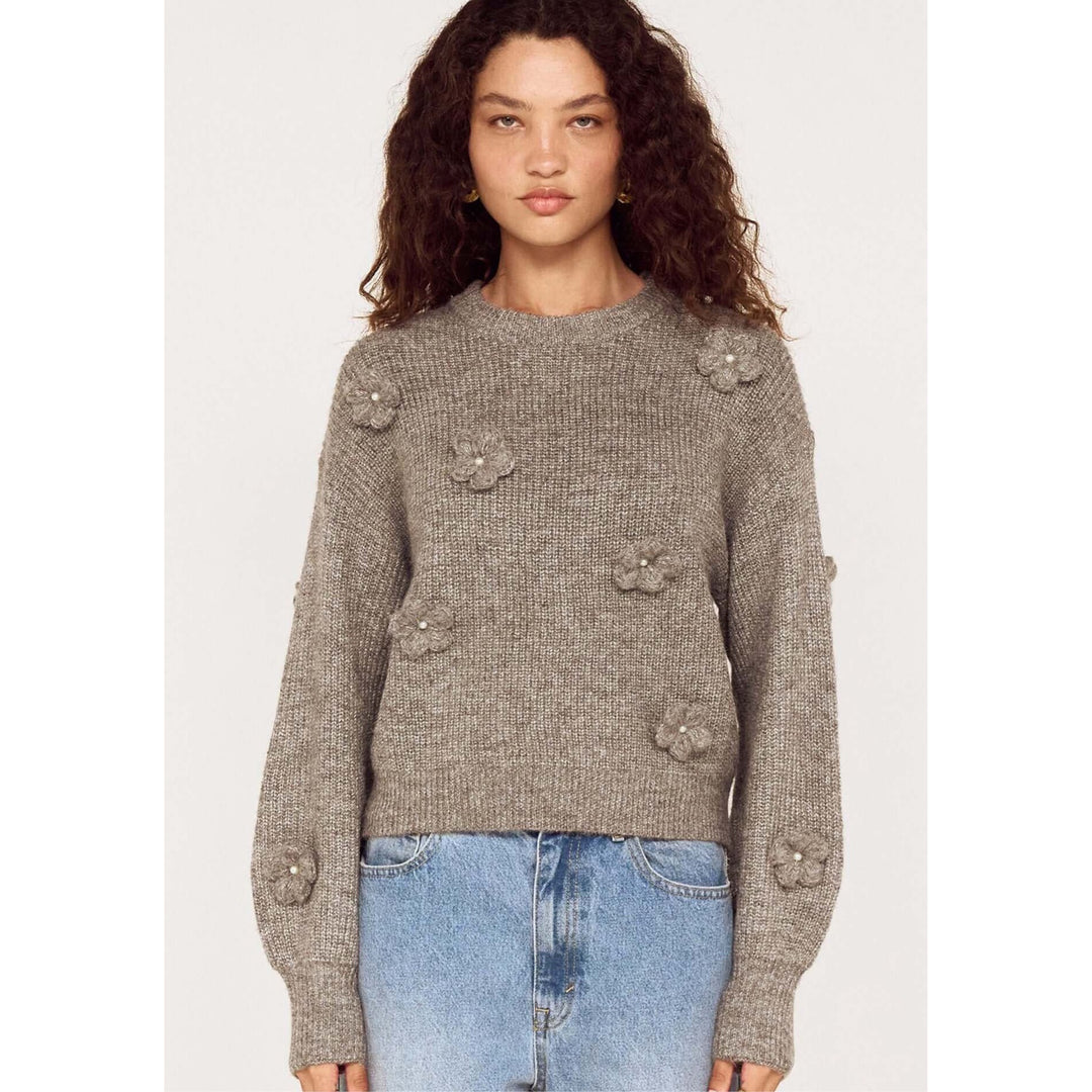 Woman wearing a gray sweater with floral embellishments on a white background