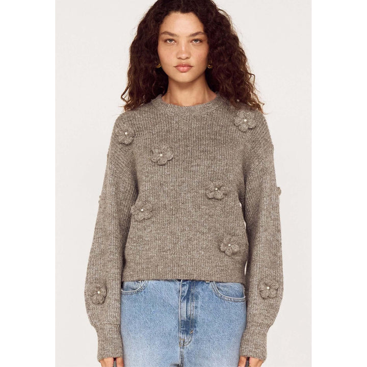 Woman wearing a gray sweater with floral embellishments on a white background