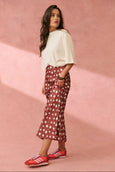 Woman wearing a white top and red polka dot pants with red shoes on a pink background