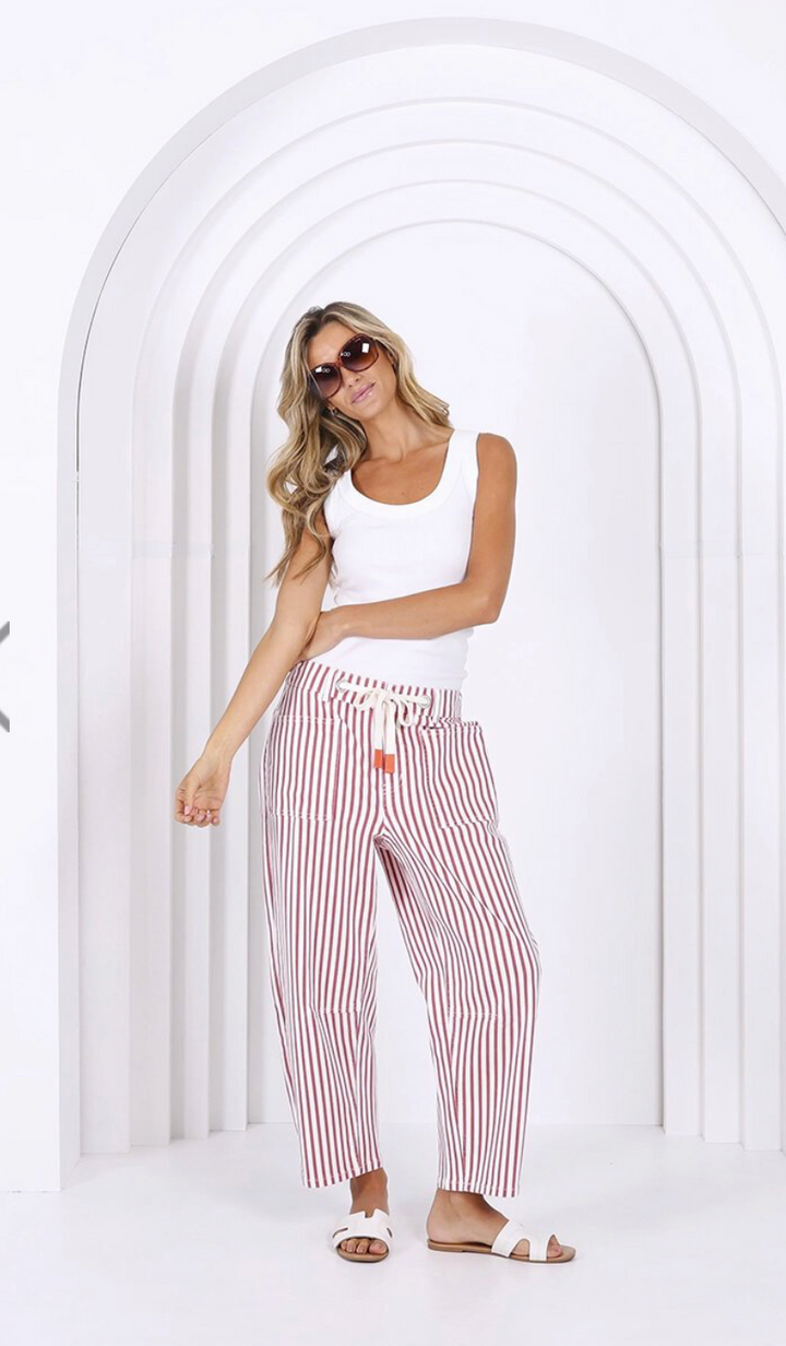 Woman wearing a white tank top and red and white striped pants standing in front of a white archway.