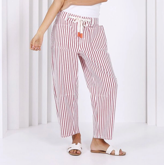 Woman wearing a white tank top and red striped pants standing in front of a white archway.