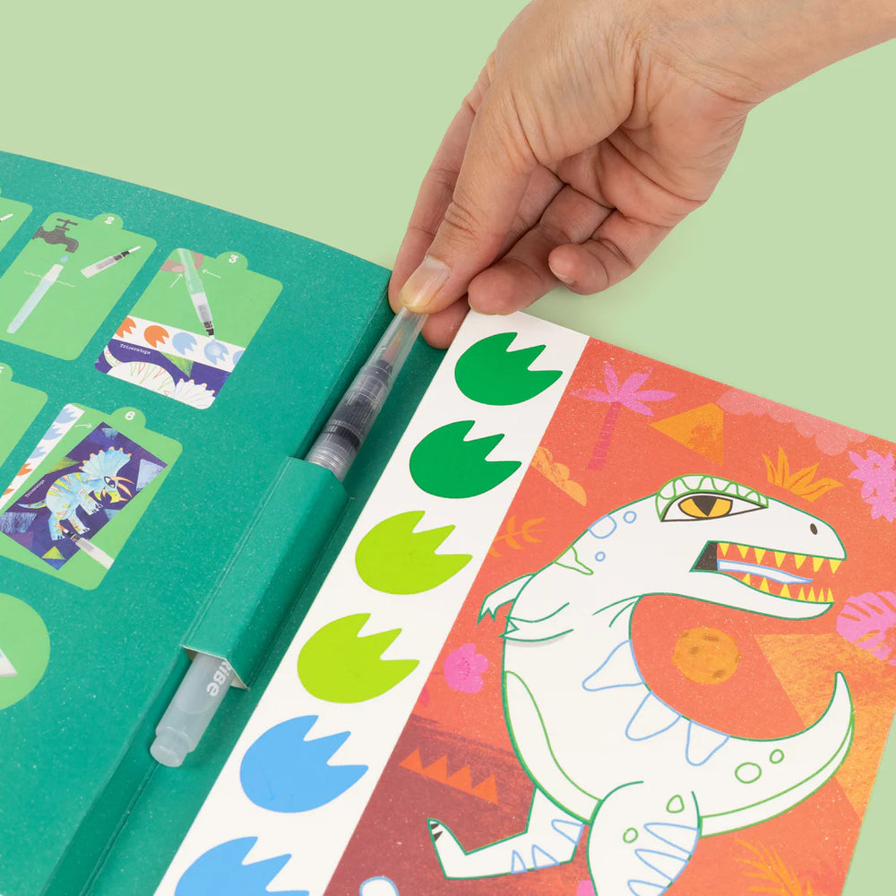 Hand applying green stickers to a colorful book with dinosaur illustrations.