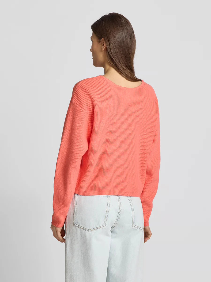 Person wearing a coral sweater and light blue jeans on a plain background