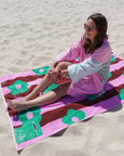 Woman sitting on a colorful towel with floral patterns on a sandy beach.