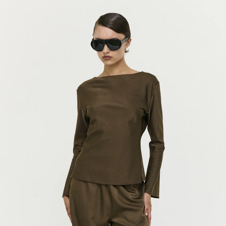 Woman wearing a brown long-sleeve top and pants with sunglasses on a light gray background