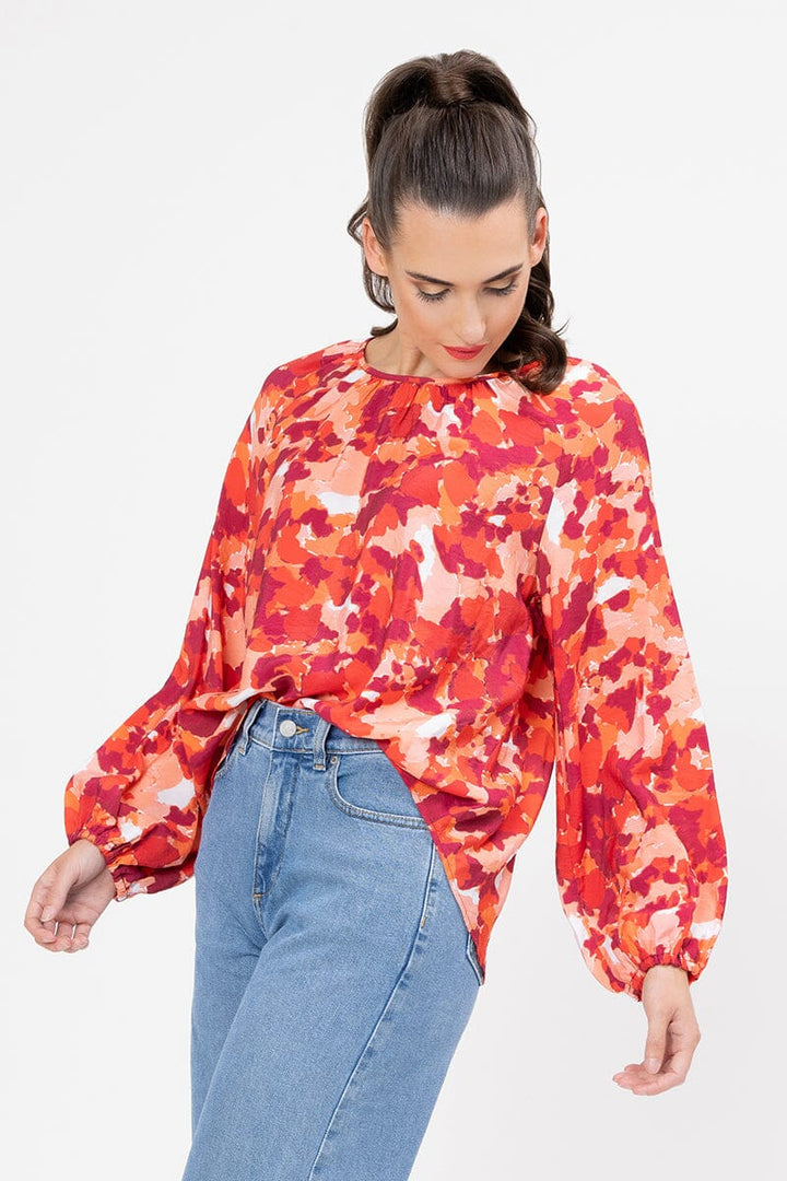 Woman wearing a colorful blouse with long sleeves and blue jeans on a white background